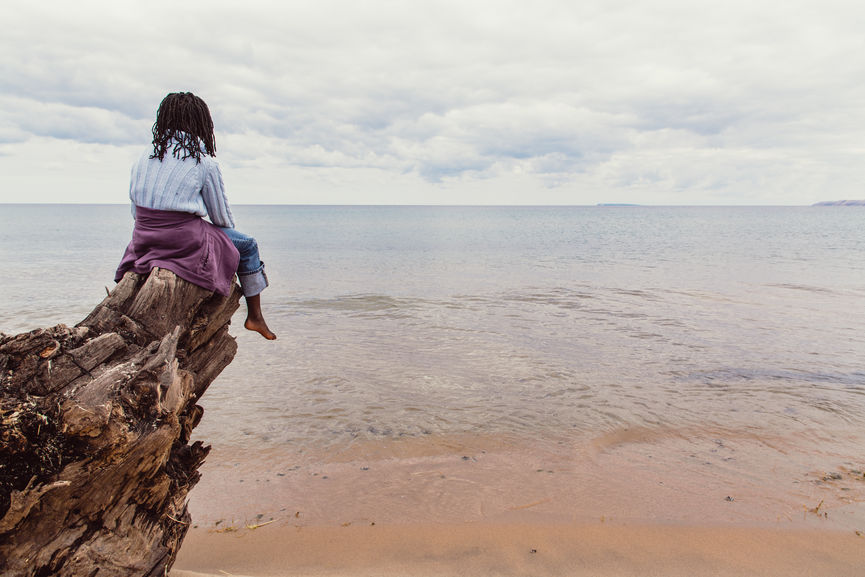 African American Girl Sitting On A Tree Log Looking Over The Sea
